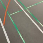 Ausschnitt von einem grauen Boden in einer Turnhalle mit grünen, roten und weissen Linien.